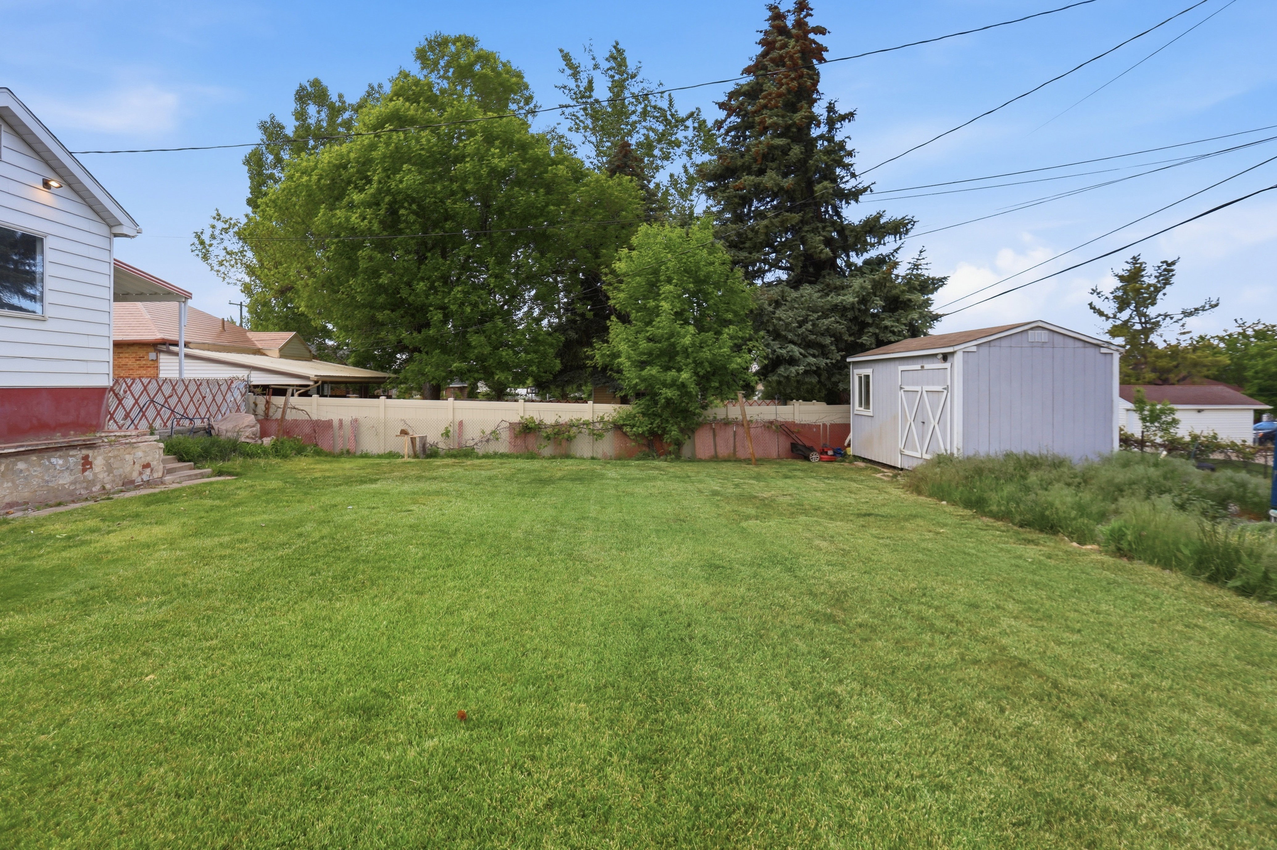 Expansive backyard featuring a green lawn, mature trees, and a detached storage shed