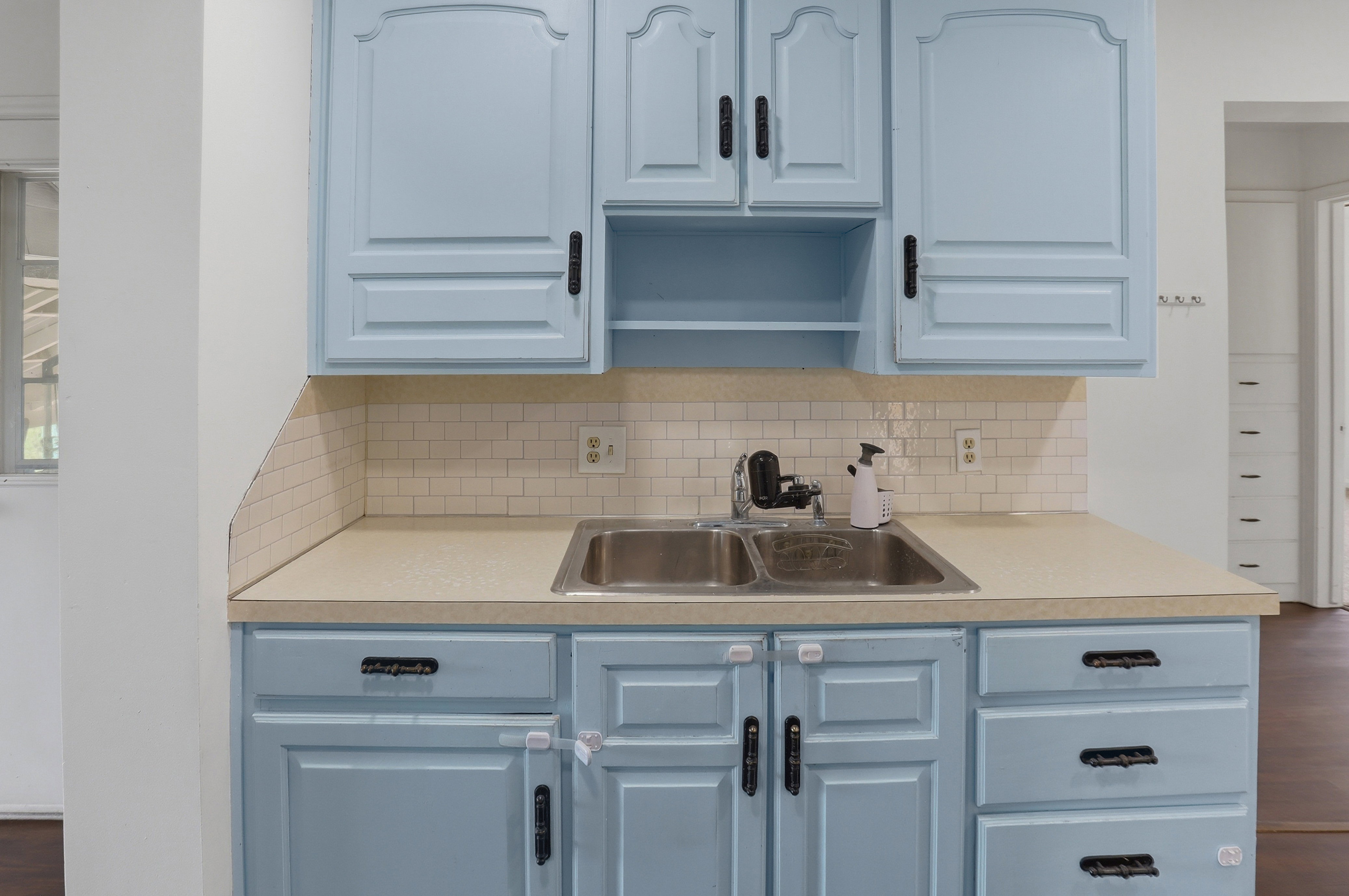 Kitchen area featuring light blue cabinetry with black hardware, a double basin stainless steel sink, and a white subway tile backsplash
