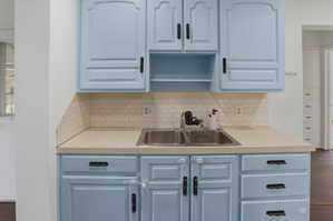 Kitchen area featuring light blue cabinetry with black hardware, a double basin stainless steel sink, and a white subway tile backsplash