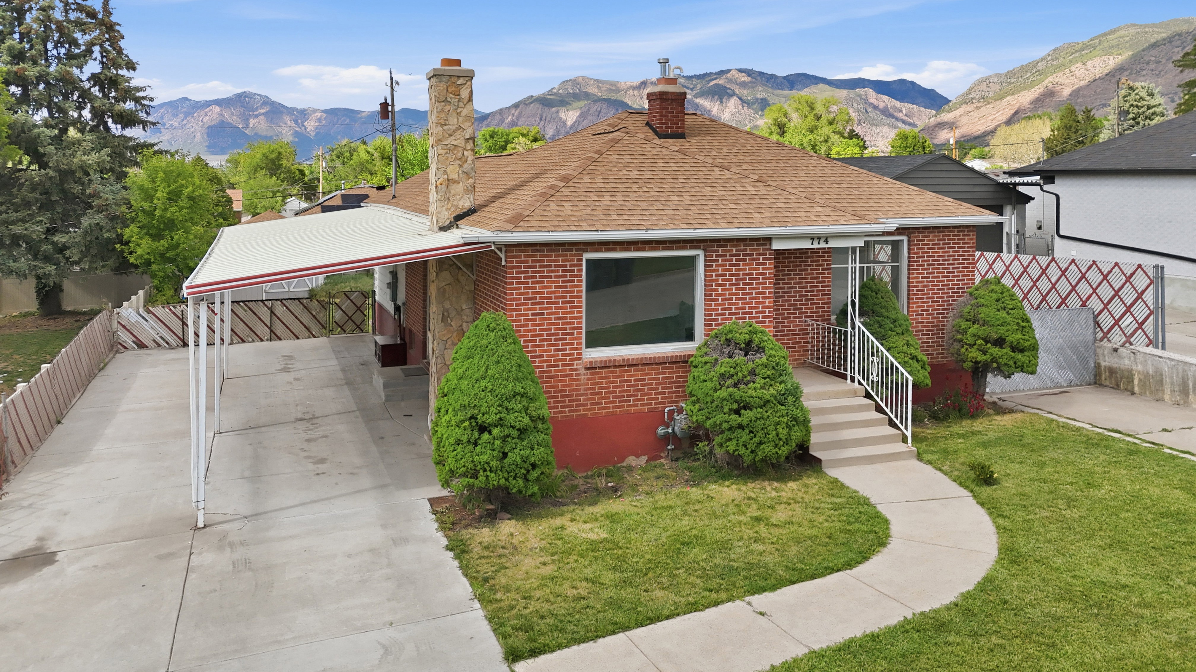 Brick exterior residence featuring a brown shingle roof, a covered carport, and a concrete pathway leading to the front entry