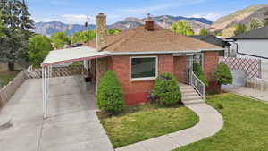 Brick exterior residence featuring a brown shingle roof, a covered carport, and a concrete pathway leading to the front entry