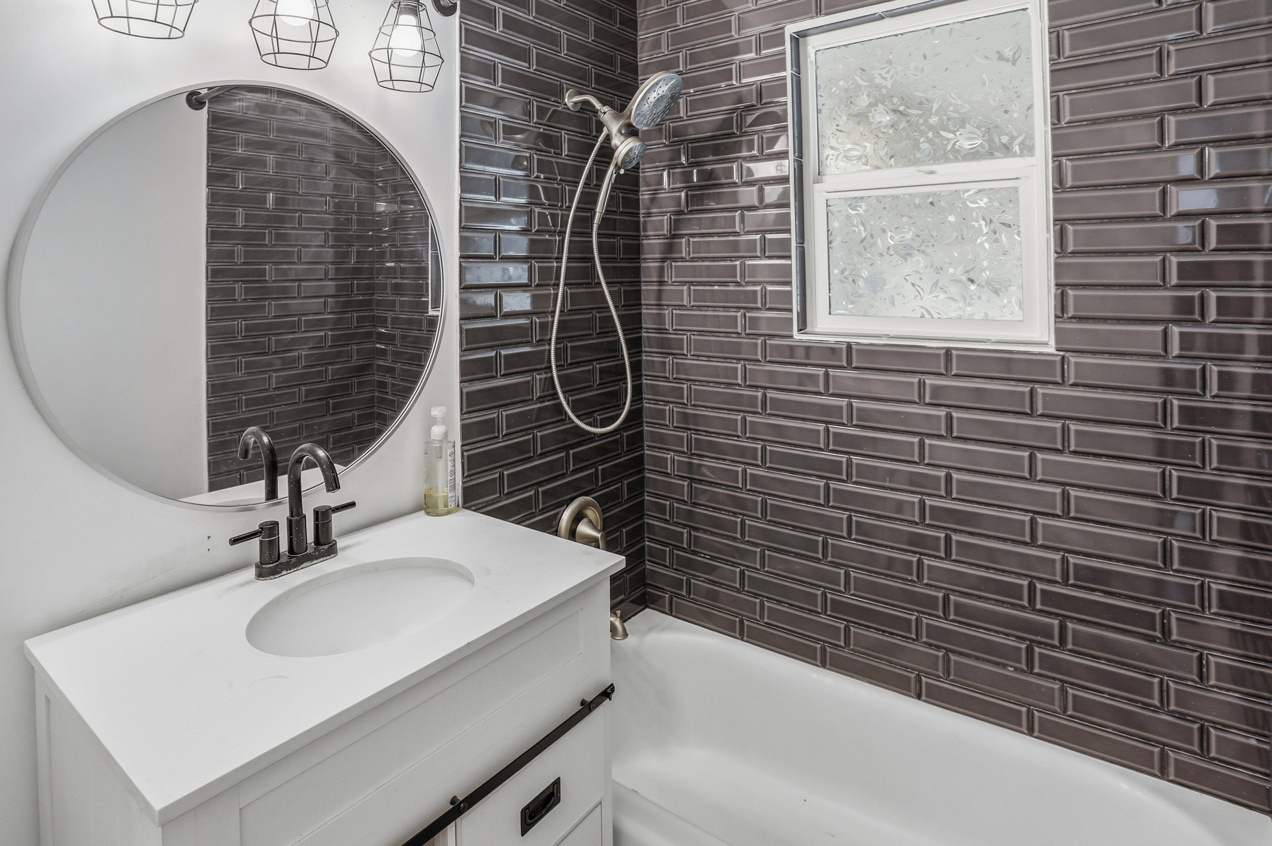 Bathroom featuring dark subway tile shower surround, white bathtub, and a modern vanity with integrated sink