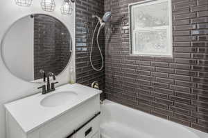 Bathroom featuring dark subway tile shower surround, white bathtub, and a modern vanity with integrated sink