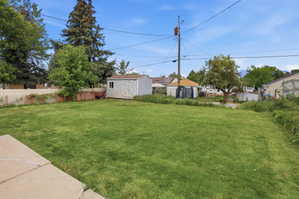 Expansive green lawn area featuring a detached storage shed, mature perimeter trees, and a partial privacy fence