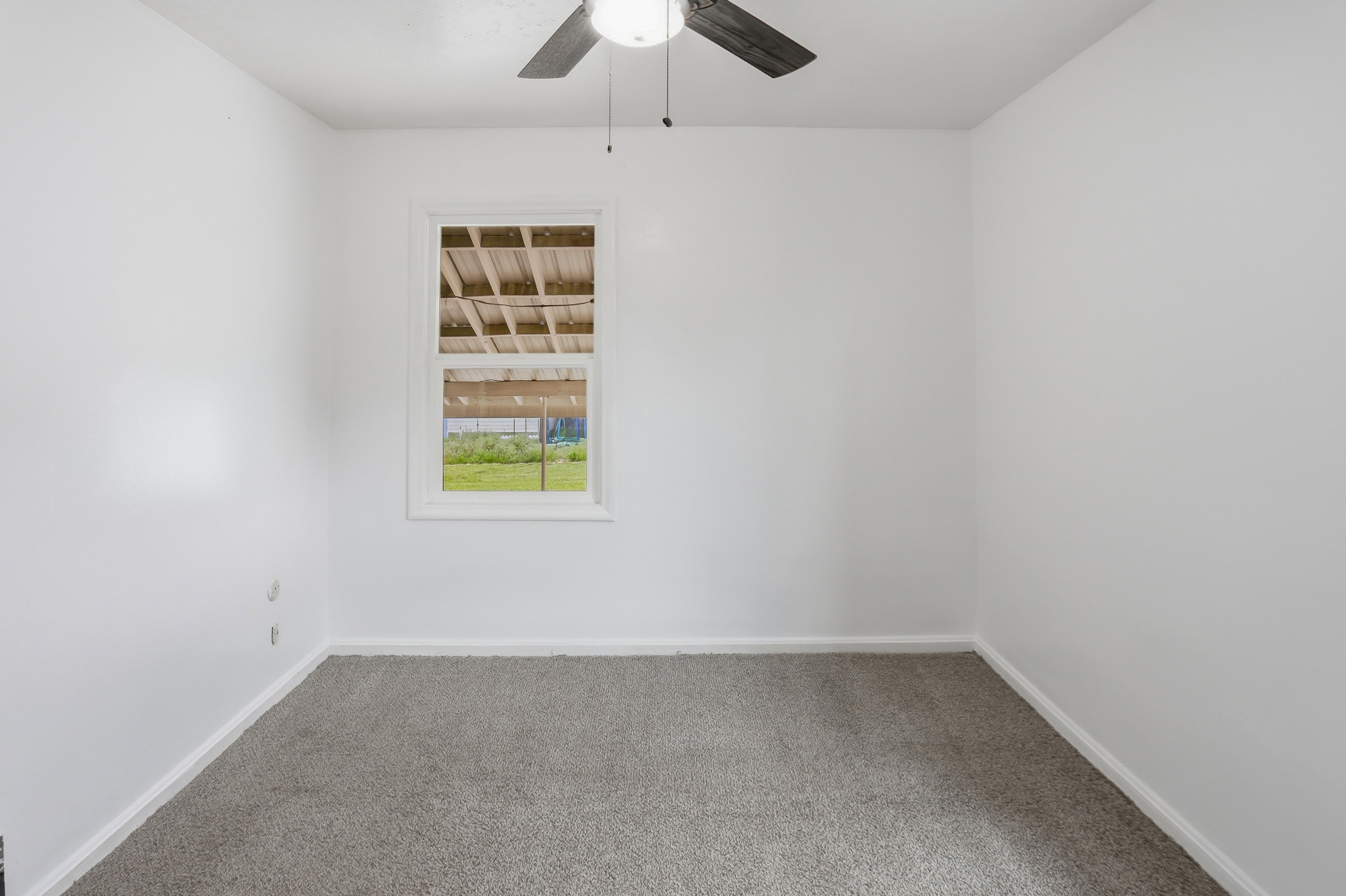Room featuring light gray carpeting, crisp white walls, a white-framed window, and a ceiling fan with dark wood-finish blades