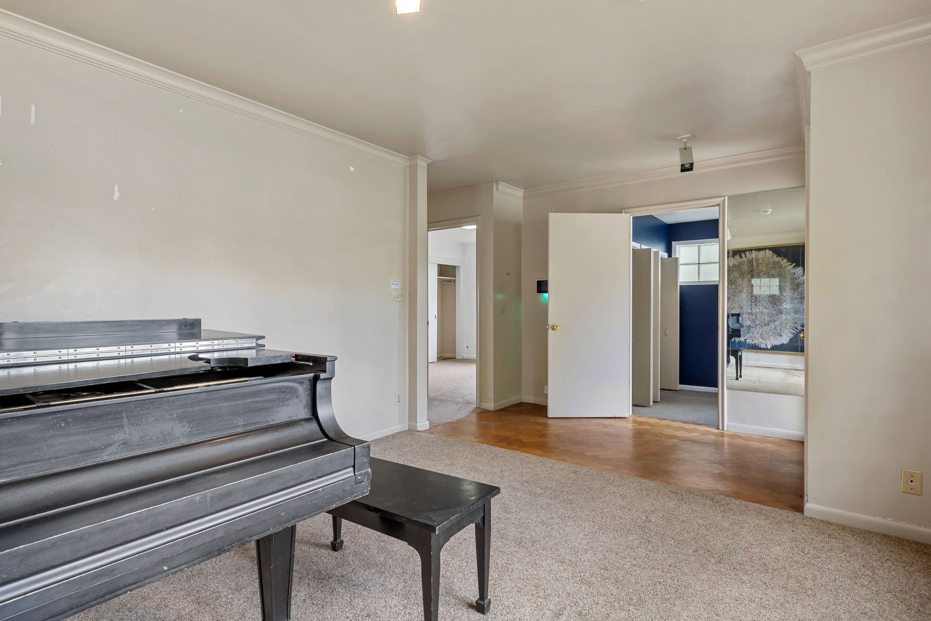 Spacious interior room featuring crown molding, neutral wall tones, and mixed flooring with carpeting and wood-finish sections
