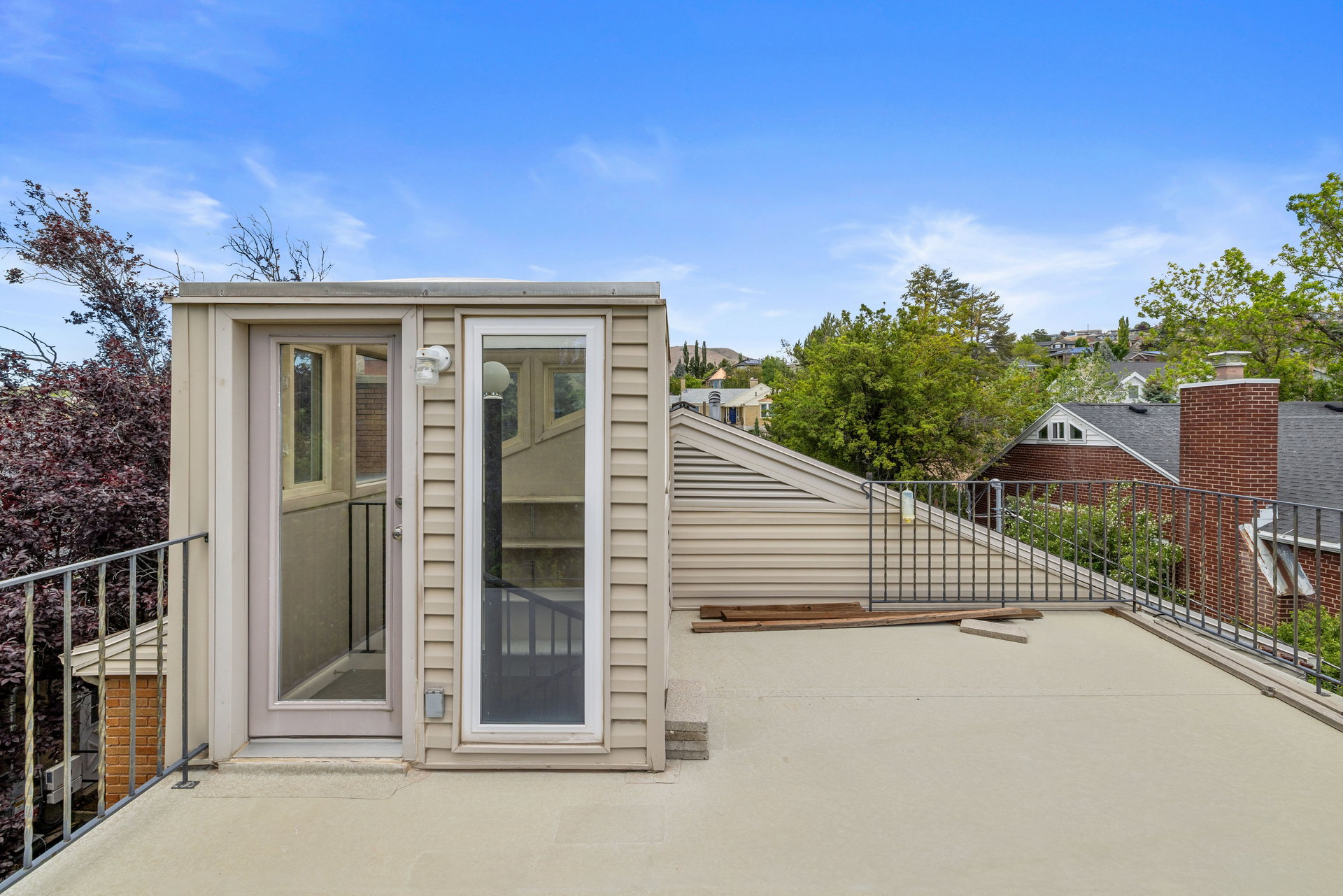 Rooftop deck featuring a light-colored surface, metal railing, and a light-sided structure with glass doors accessing interior stairs