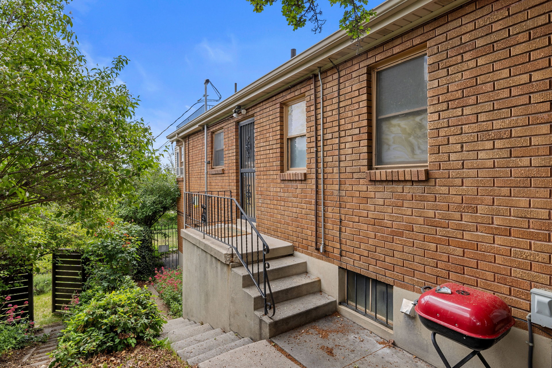 Brick exterior with multiple window openings and a concrete staircase leading to a secured entry door