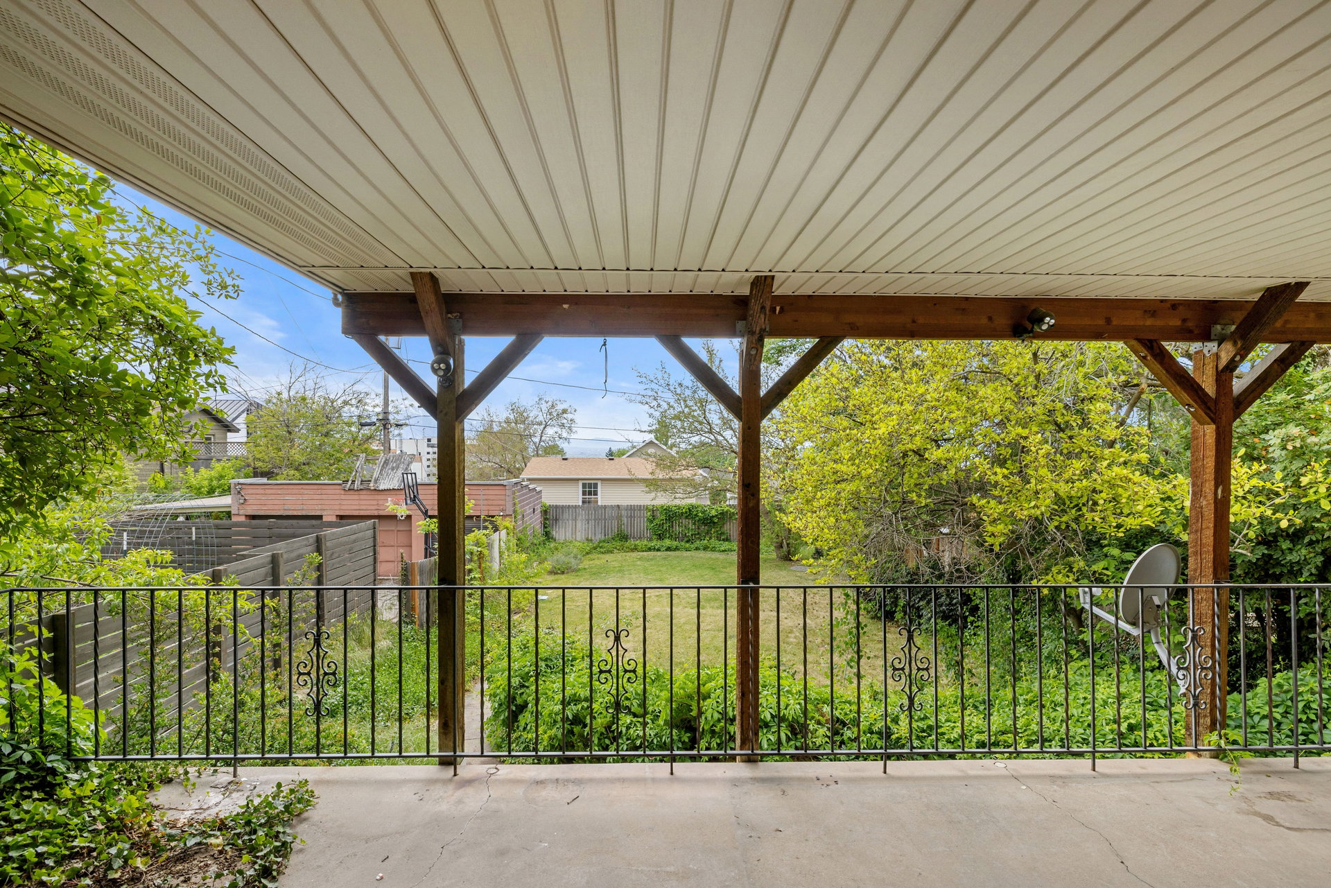 Covered patio with a concrete surface, supported by exposed wood beams, featuring a decorative metal railing