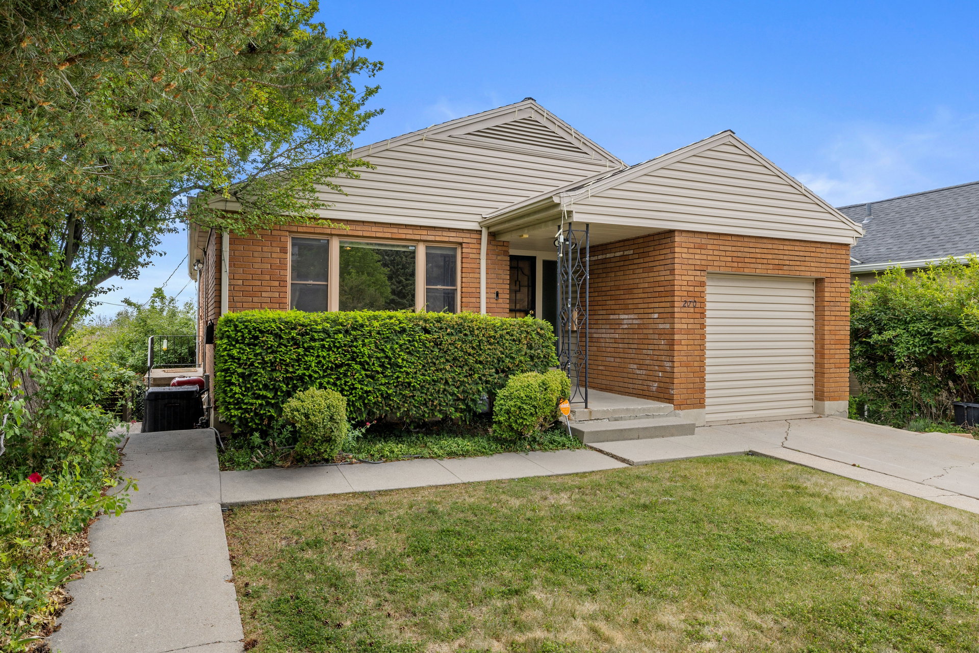 Brick and siding exterior with an attached garage, covered entryway, mature landscaping, and a concrete driveway