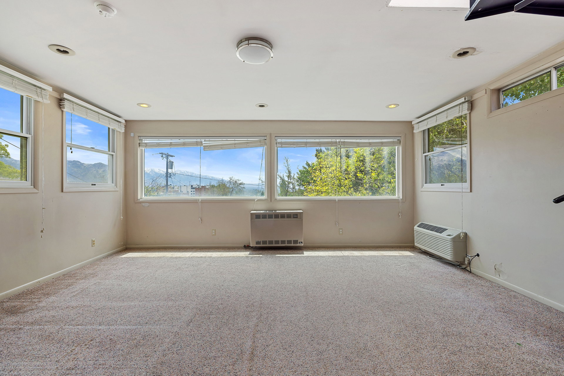 Carpeted room with multiple windows, recessed lighting, and wall-mounted heating/cooling units