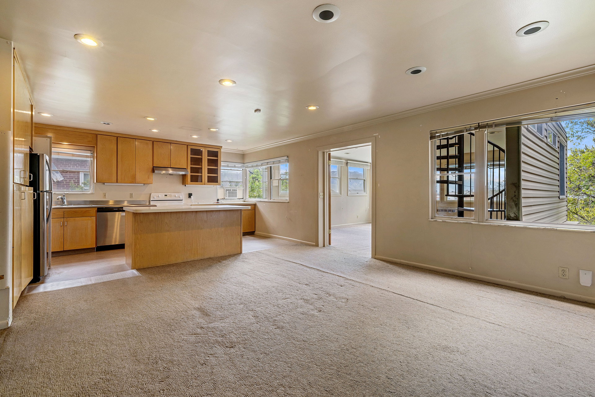 Open-concept living space featuring a kitchen with light wood cabinetry, stainless steel appliances, and a central island