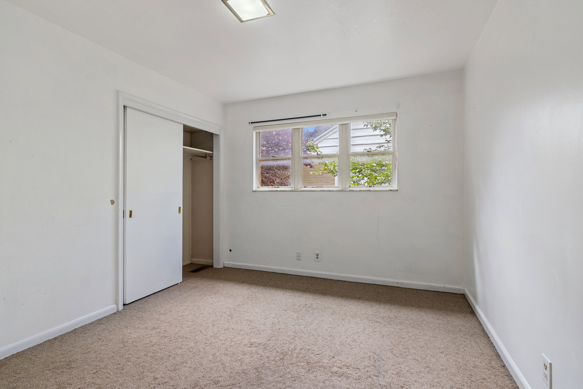Carpeted room featuring a window with exterior views, white walls, and a built-in closet with sliding doors
