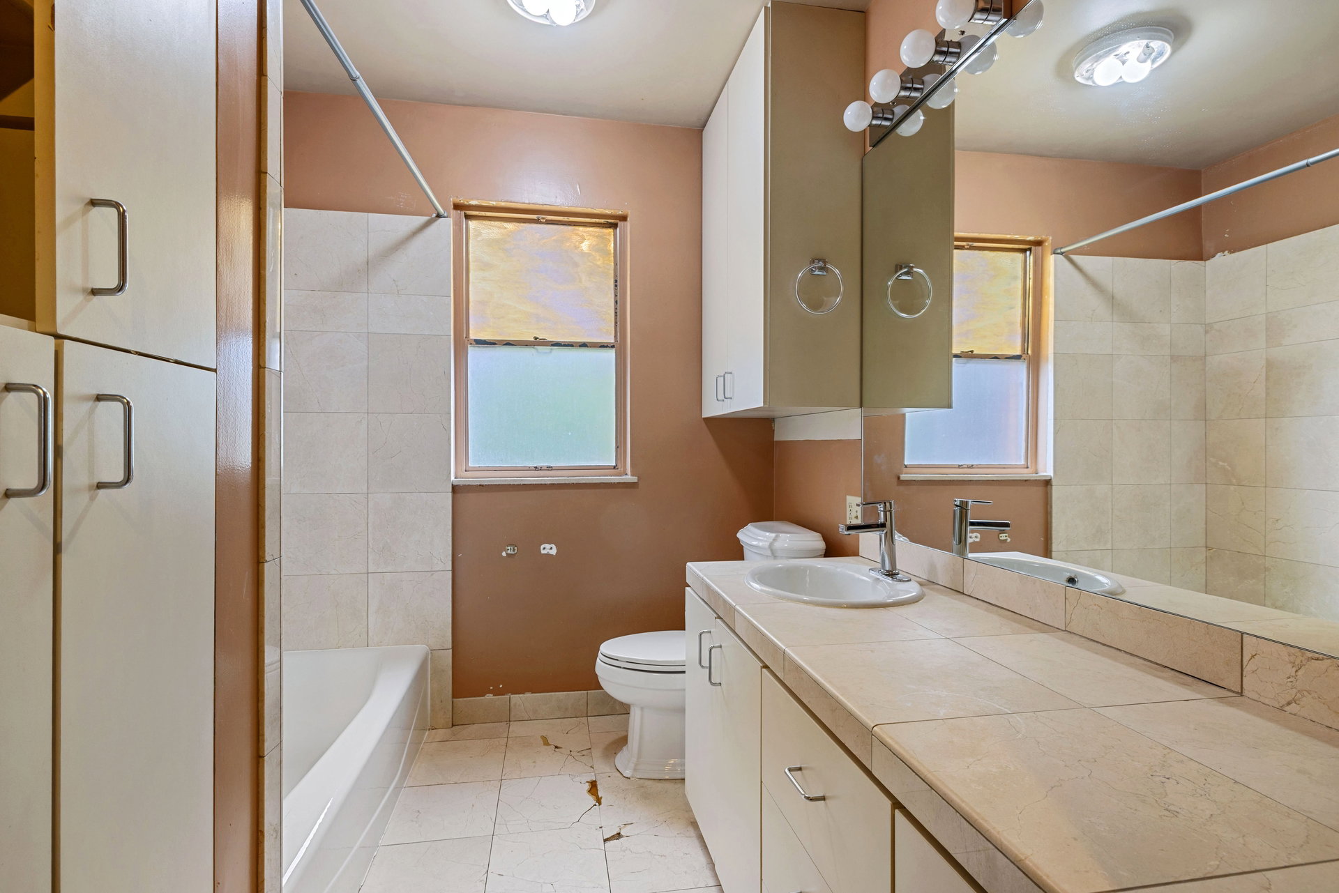 Bathroom featuring a full-width vanity with an integrated sink, a large mirror, and overhead cabinet storage