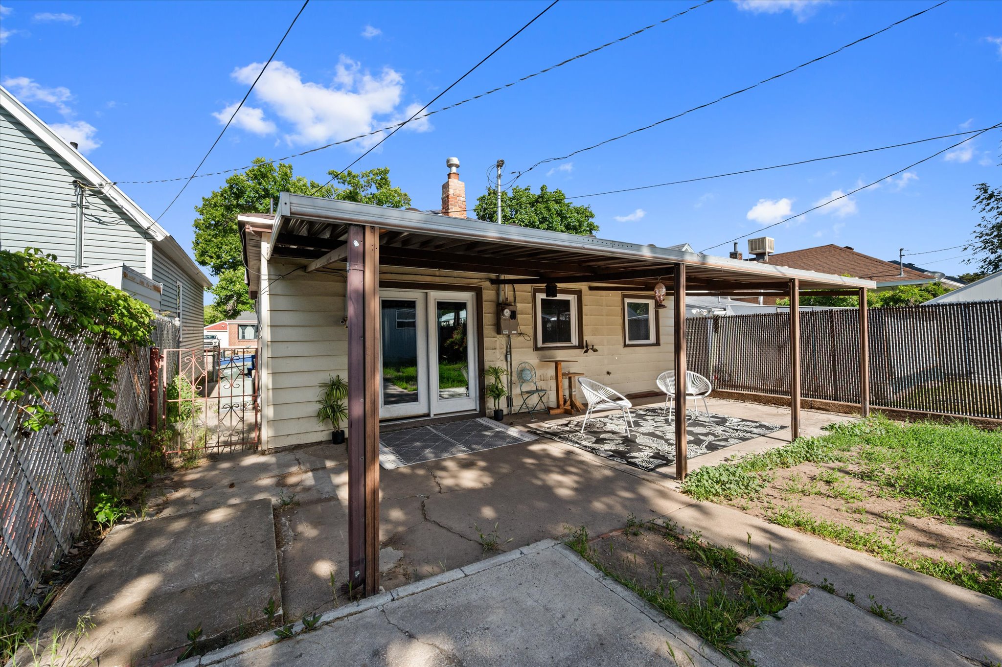 Rear patio area featuring a covered outdoor space with concrete flooring, a dual-pane patio door, and a partially fenced yard