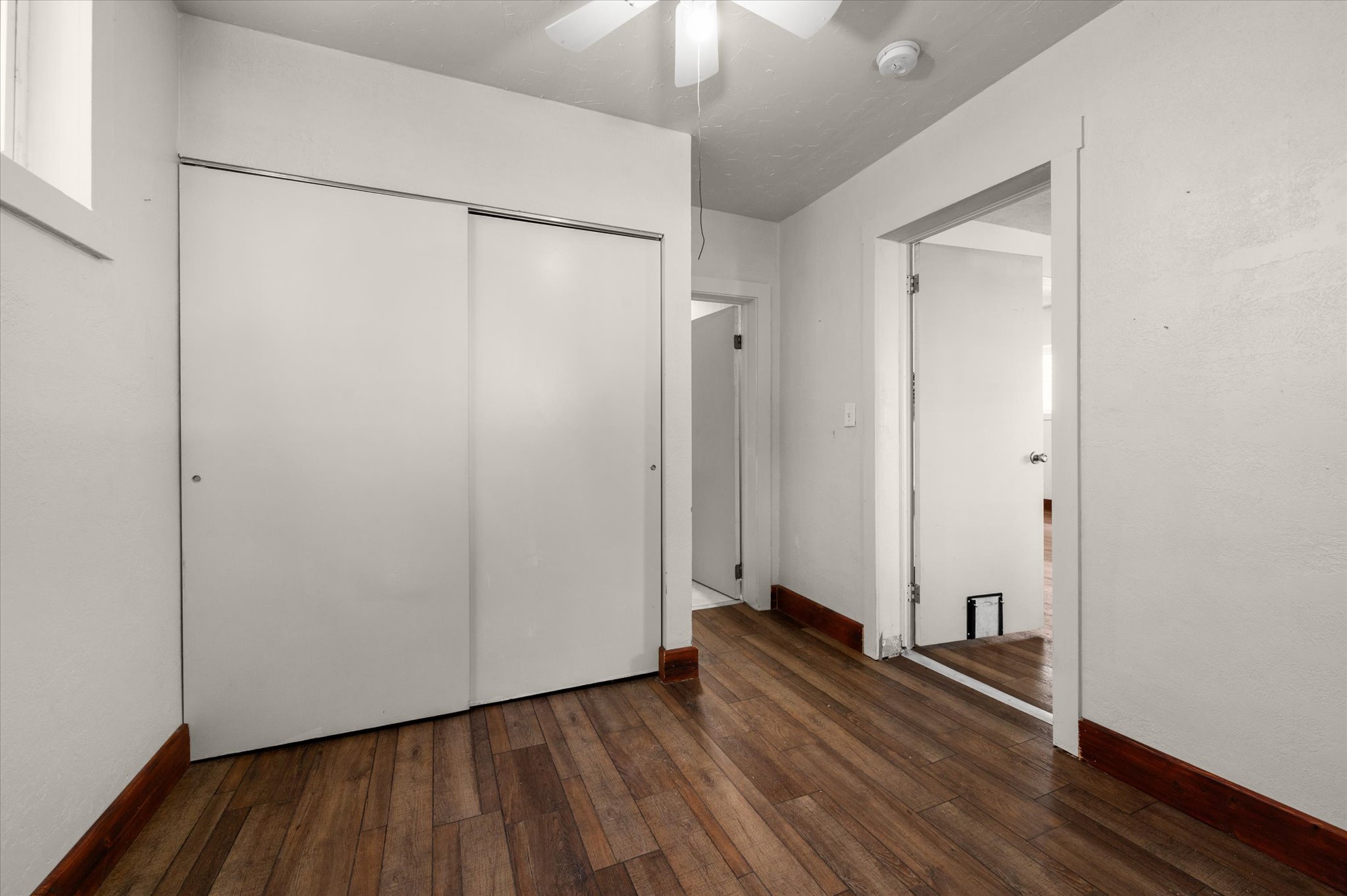Interior room featuring wood-finish flooring, white walls, and a white ceiling fan