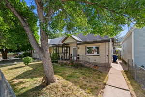 Exterior featuring a prominent mature shade tree, a covered porch with decorative railings, and a concrete walkway