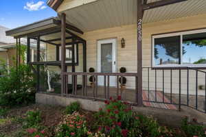 Inviting front porch featuring a white entry door, exterior wall lantern, and numerical address display