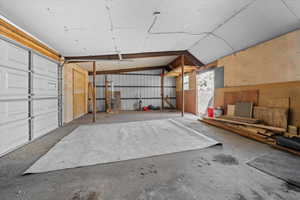 Spacious garage with concrete flooring, overhead garage door, exposed beam ceiling, and mixed wall finishes including plywood and corrugated metal