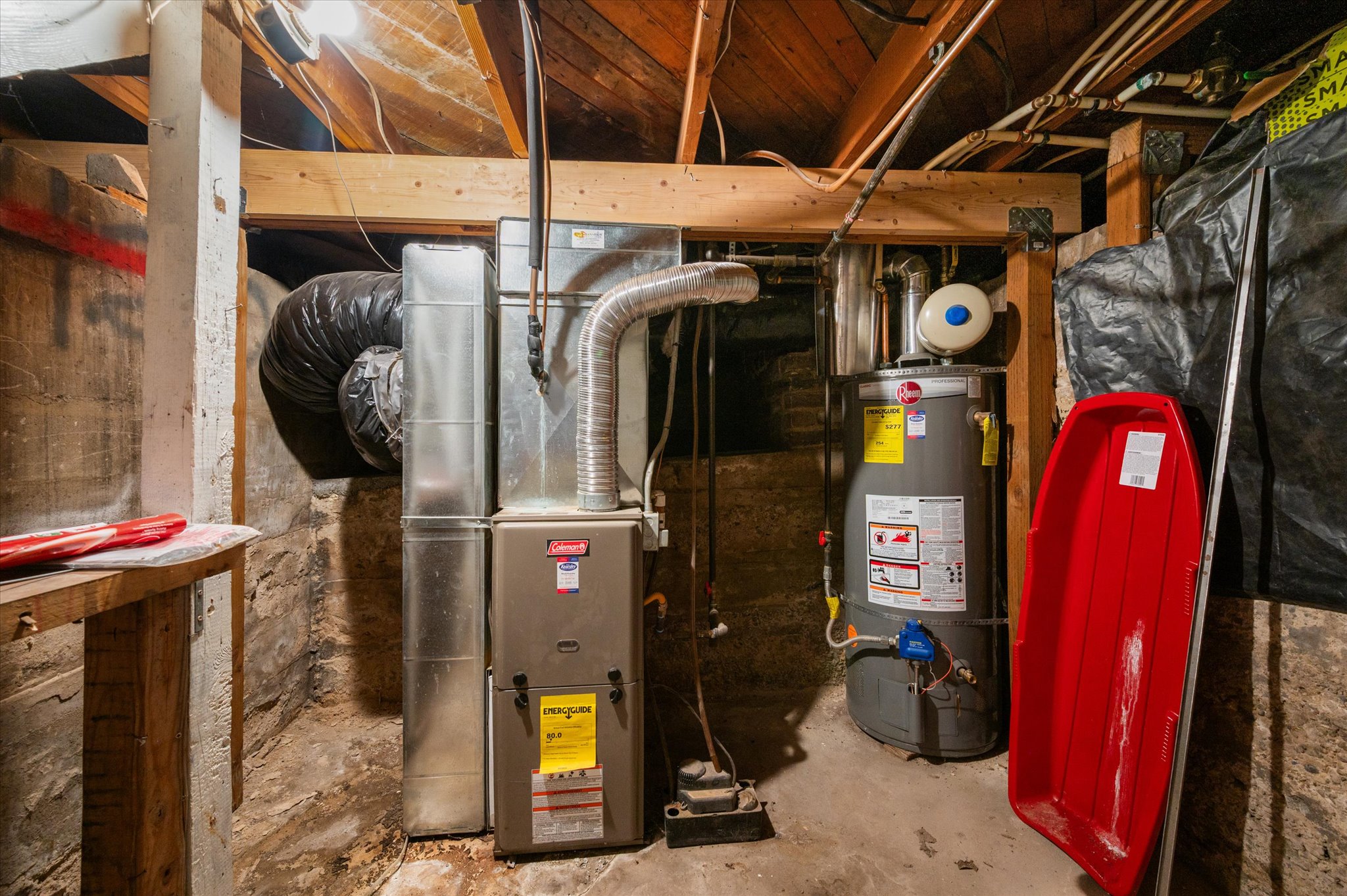 Central furnace with associated ductwork and a water heater, alongside exposed wooden beams and a stone foundation wall