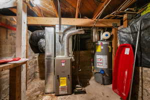 Central furnace with associated ductwork and a water heater, alongside exposed wooden beams and a stone foundation wall