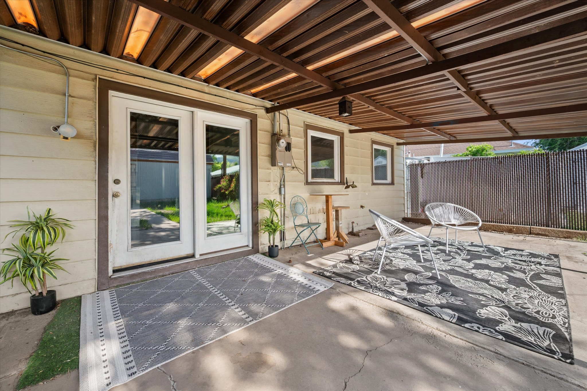 Concrete patio with a wood-slat overhead covering, dual-pane glass French doors, and two windows with white trim