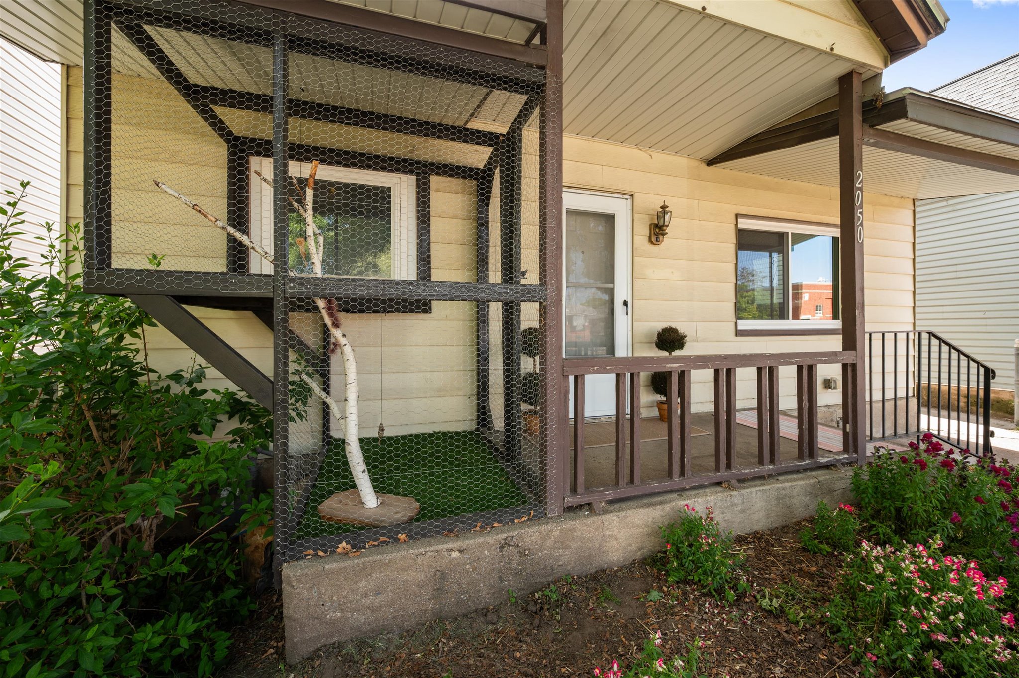 Covered front entry porch with horizontal siding, an exterior wall sconce, and a wood railing