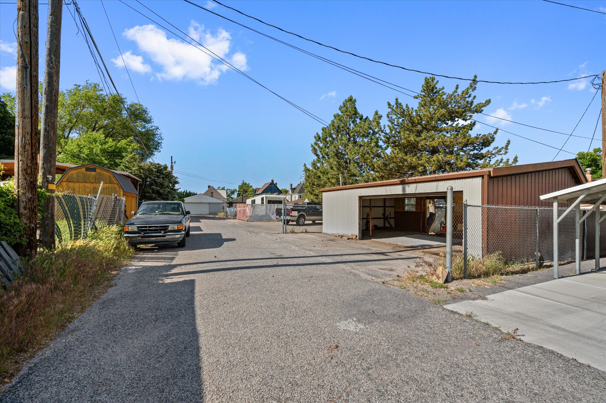 Detached metal carport structure with two open bays, an additional enclosed structure, and a fenced perimeter