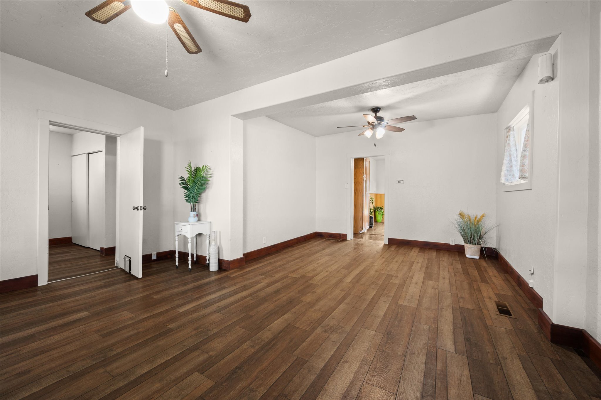 Spacious interior room featuring wood-finish flooring, white walls, and a ceiling fan
