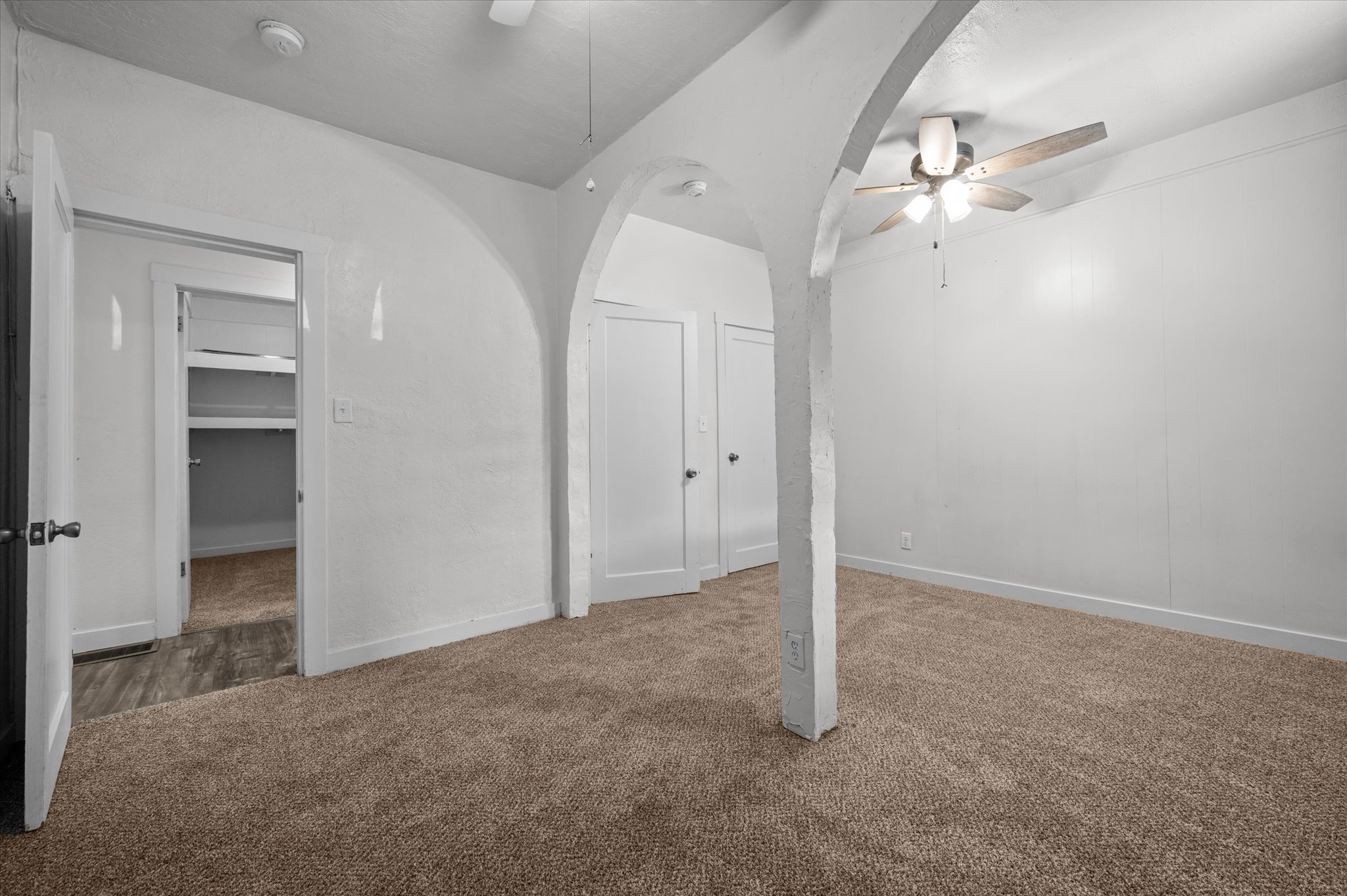 Carpeted room featuring a ceiling fan, arched architectural elements, and white walls