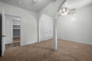 Carpeted room featuring a ceiling fan, arched architectural elements, and white walls