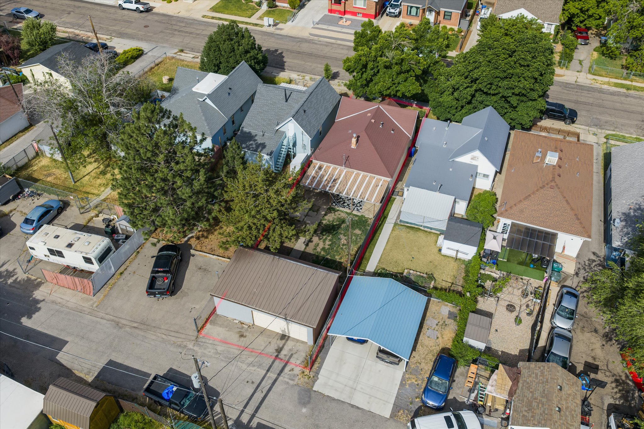 Aerial perspective showcasing a light blue residence with a dark gray roof, accompanied by a detached brown-roofed structure and a separate brown two-car garage