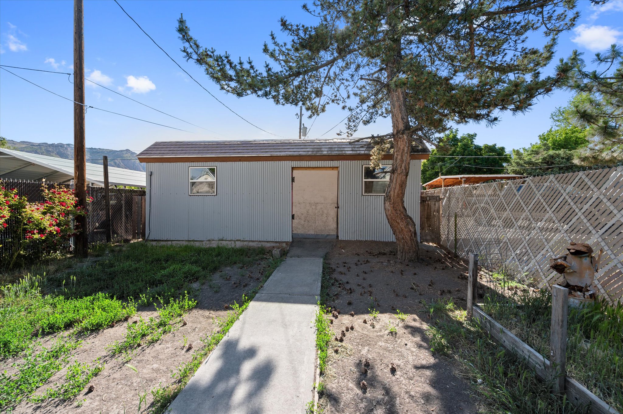 Detached storage building with corrugated metal siding, a single window, and a concrete pathway