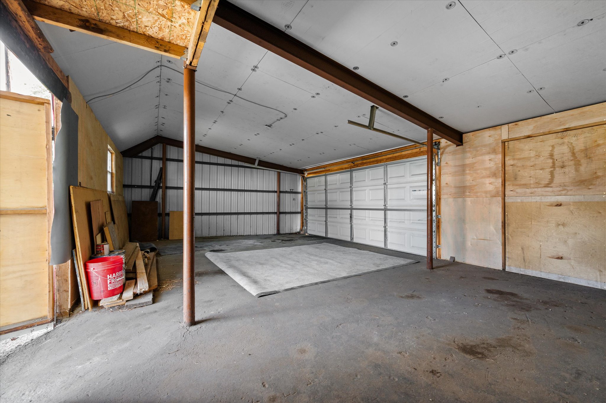 Spacious garage featuring a concrete floor, two white paneled garage doors, exposed metal beams, and a vaulted ceiling