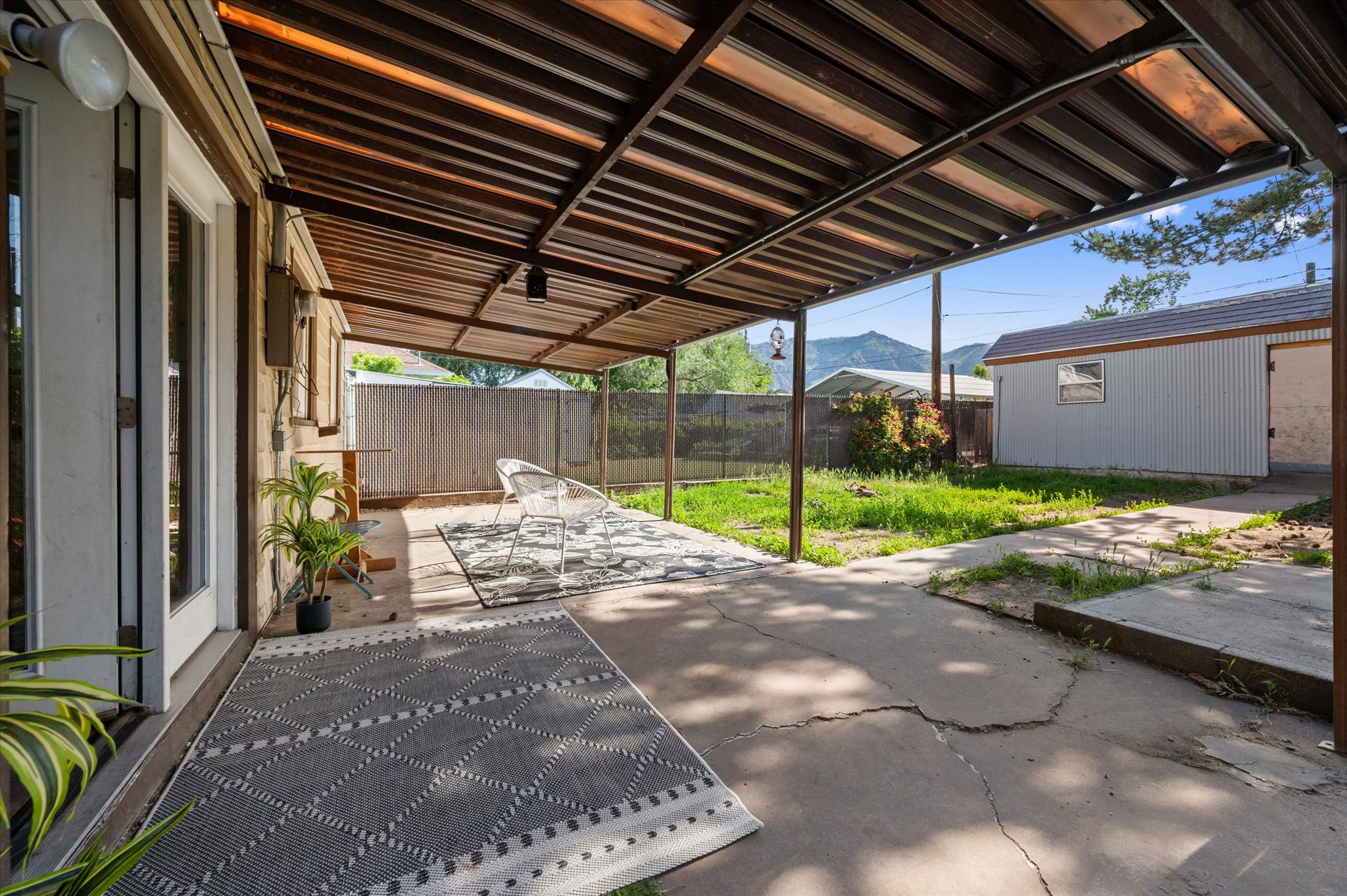 Covered patio with a slatted roof structure, concrete flooring, and an exterior door with glass panels
