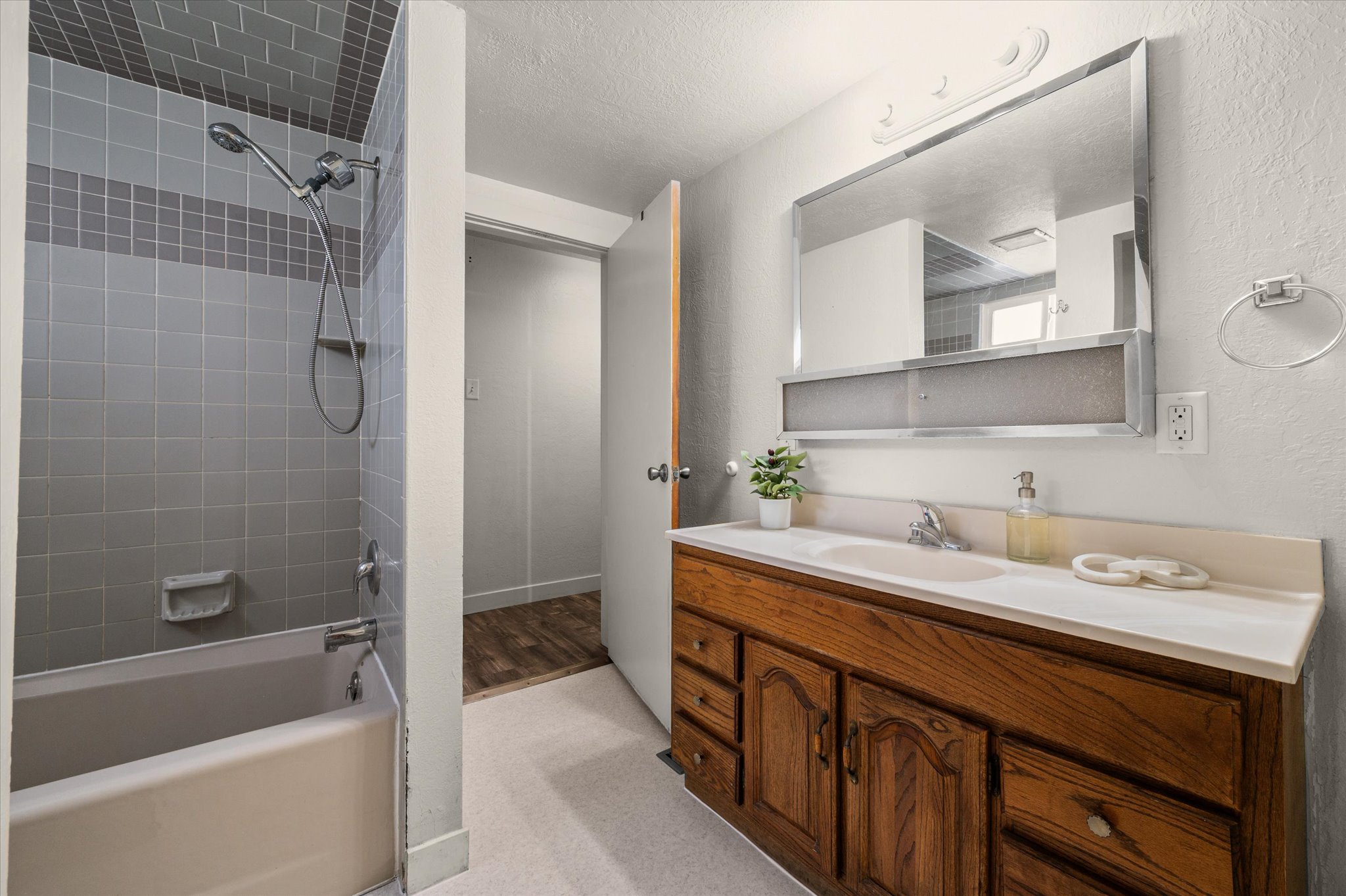 Bathroom featuring a tub/shower combination with grey tile surround, a wood-finish vanity with a single basin sink, a wall-mounted mirror, and a towel ring