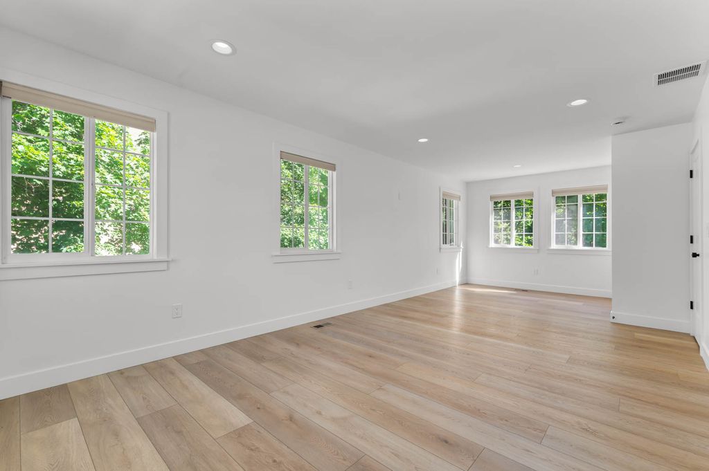 Spacious room featuring light wood-finish flooring, recessed lighting, multiple windows with white trim, and a neutral color palette