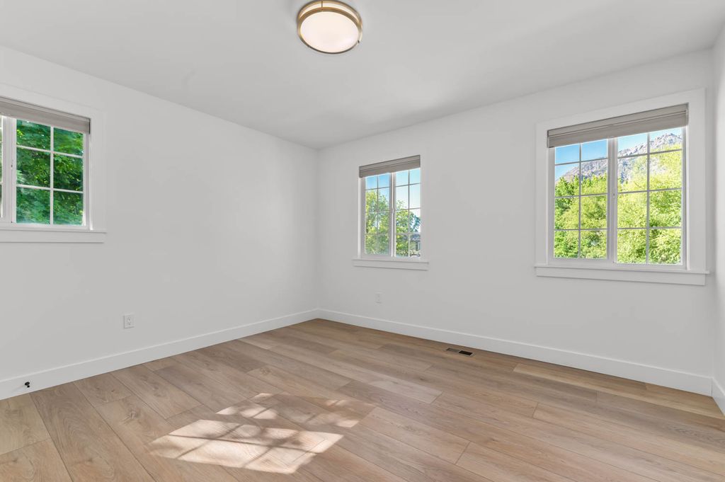 Bright room featuring multiple windows with roller shades, wood-finish flooring, white walls, and a flush-mount ceiling light