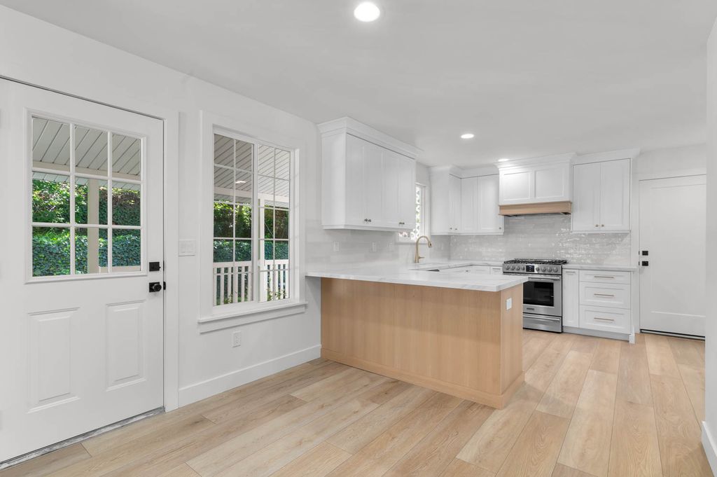 Modern kitchen featuring white cabinetry, light wood-finish flooring, a central island with a light-toned wood base, stainless steel appliances, and an intricate tile backsplash
