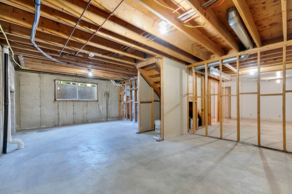 Unfinished basement featuring concrete flooring, exposed wood beam ceiling, framed interior walls, and a window with horizontal blinds