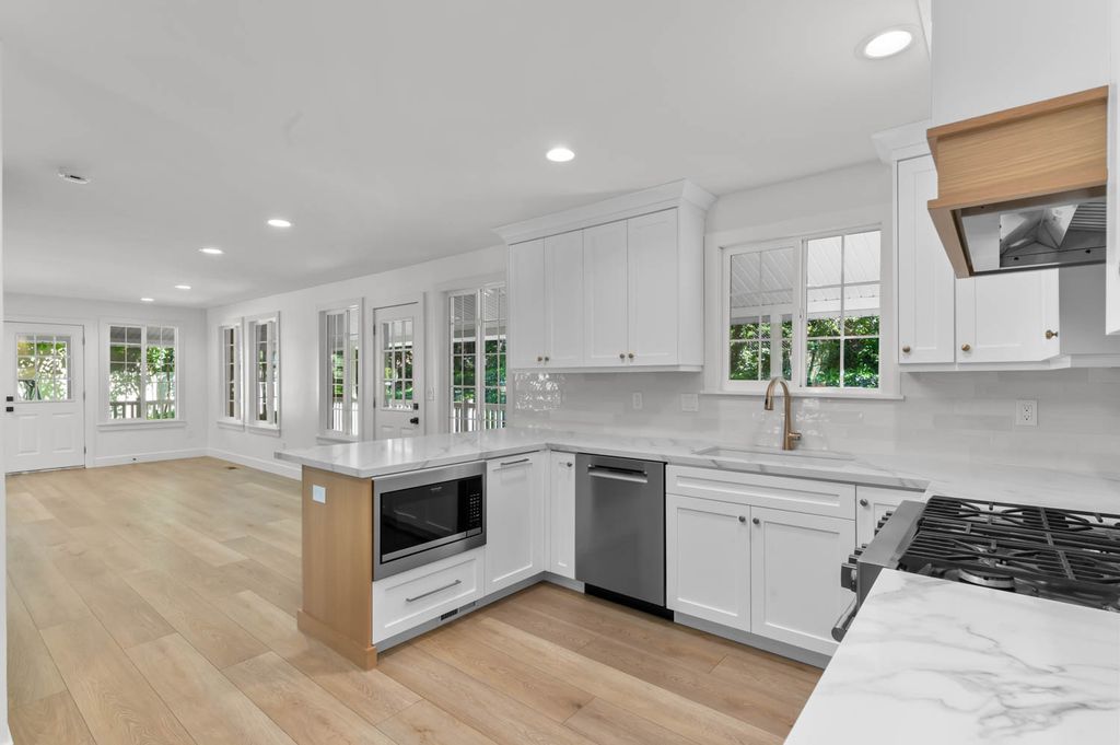 Open-concept kitchen featuring white shaker cabinetry, light wood-finish flooring, and white countertops