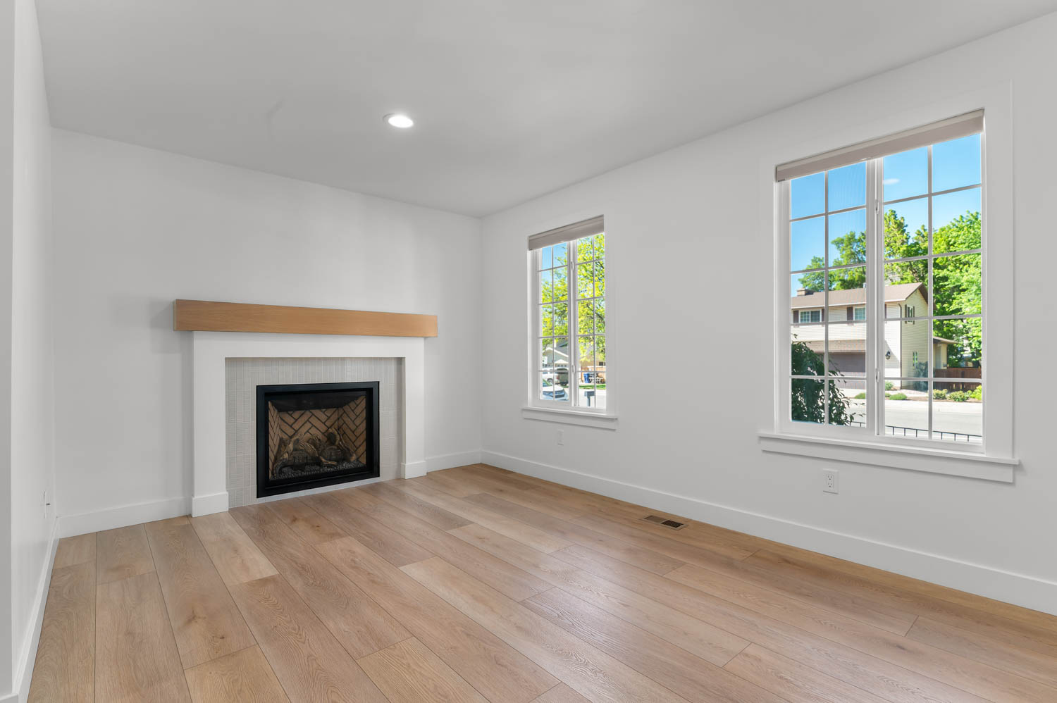 Office space featuring a white fireplace with a light wood mantel, light wood-finish flooring, two large windows, and recessed lighting