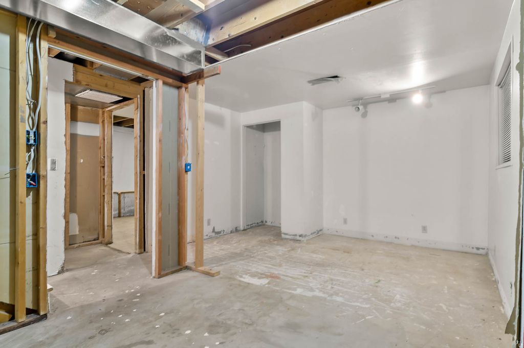 Unfinished basement space featuring exposed wooden ceiling joists, concrete flooring, and partially framed walls