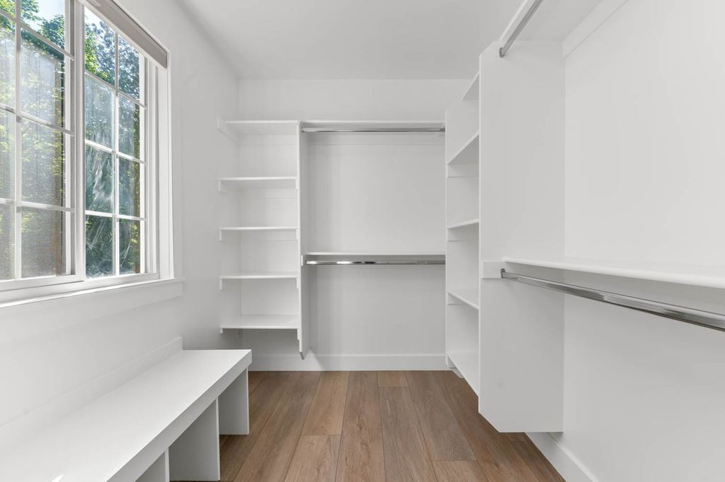 Walk-in closet featuring built-in shelving, hanging rods, an integrated window, a built-in bench, and wood-finish flooring