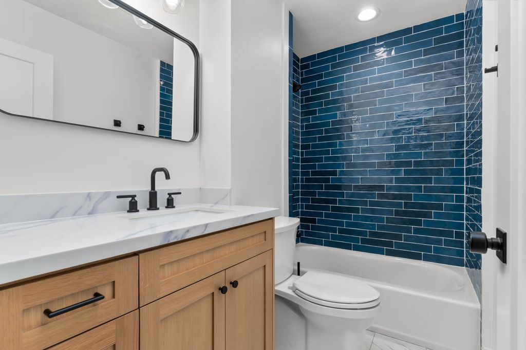 Modern bathroom featuring a wood-finish vanity with a stone-look countertop, integrated sink, and matte black fixtures