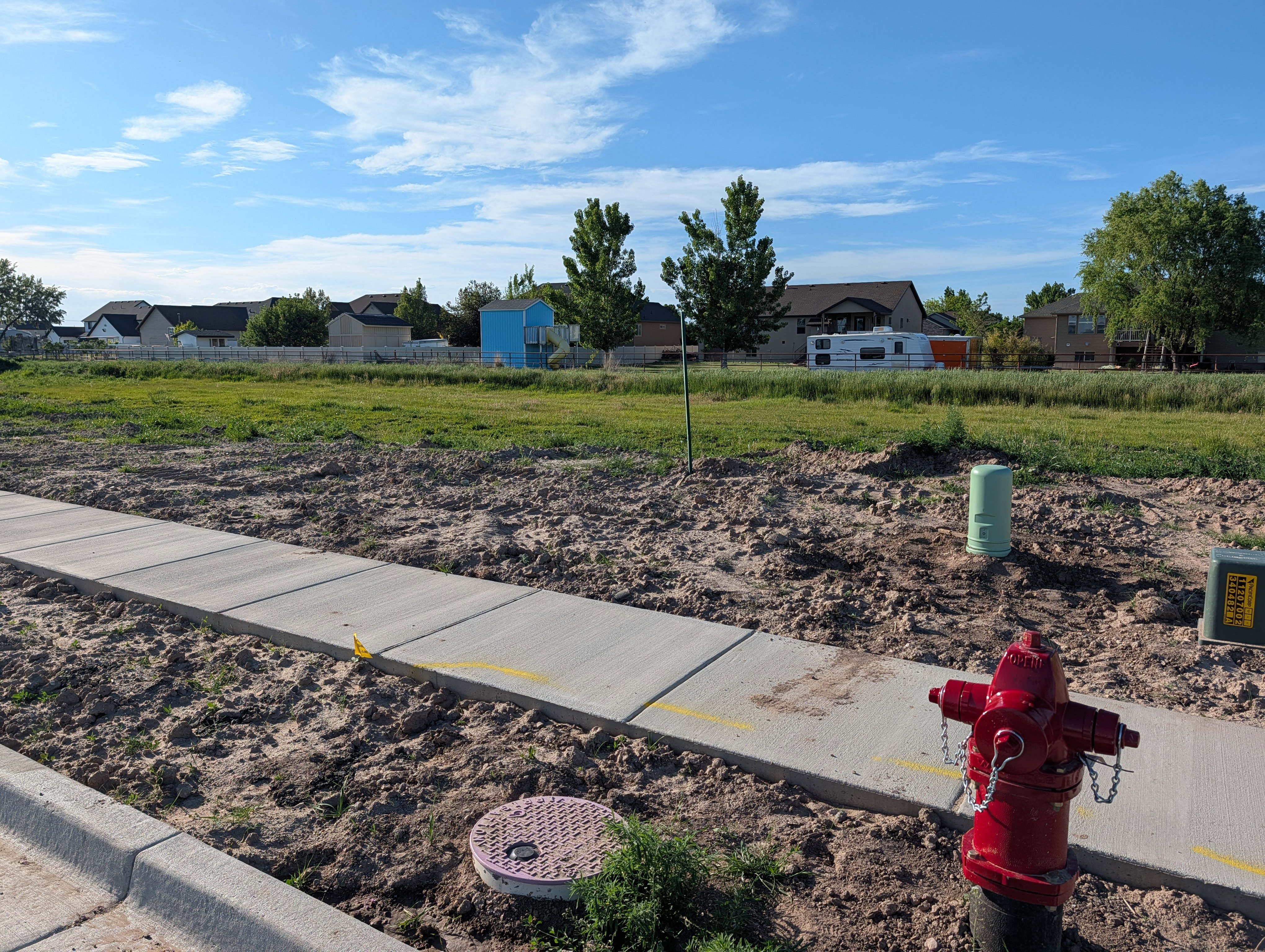 Expansive undeveloped lot featuring a newly installed concrete sidewalk and curb