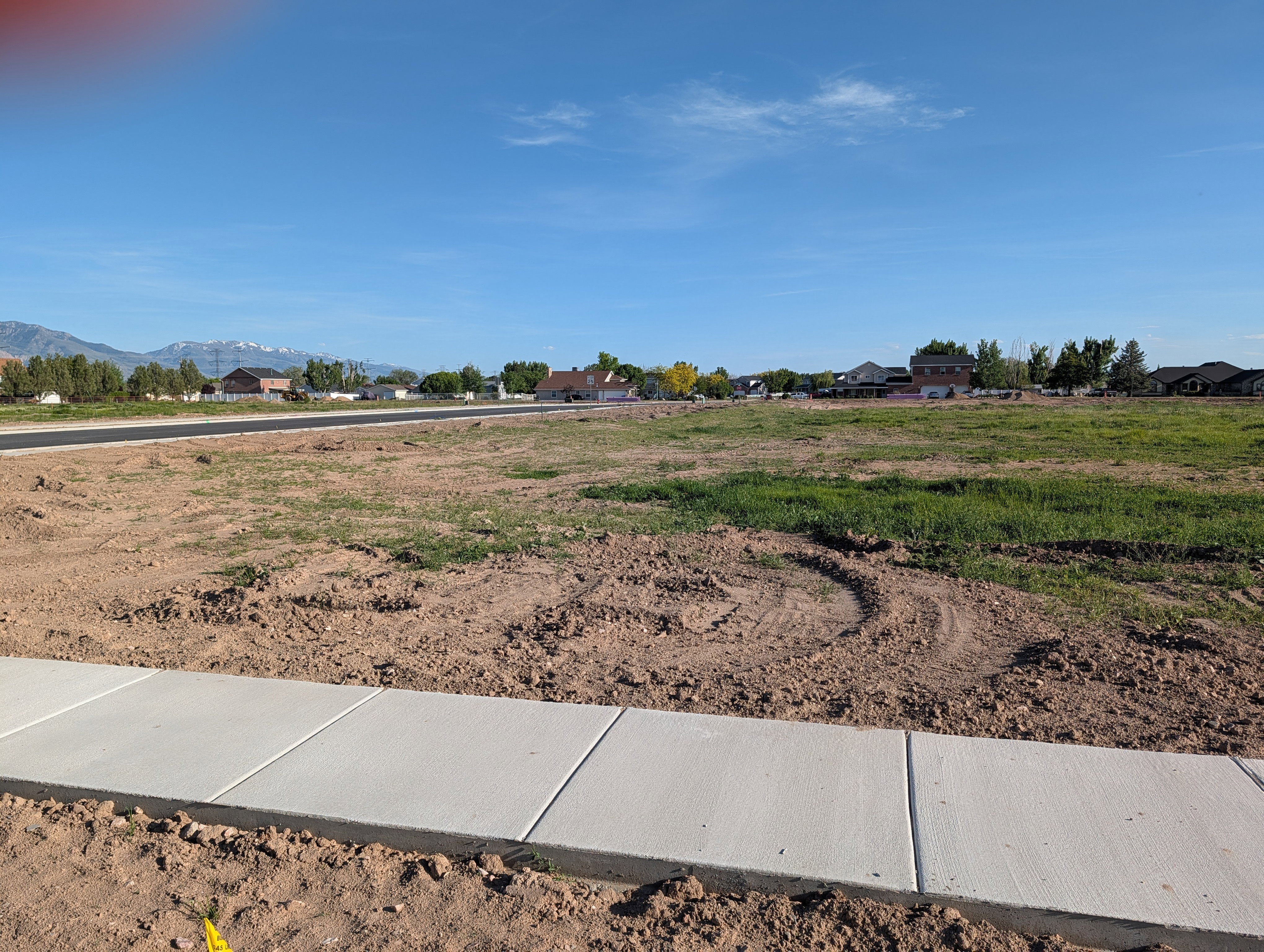 Expansive level land parcel featuring partial green ground cover and a newly installed concrete sidewalk