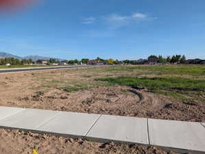 Expansive level land parcel featuring partial green ground cover and a newly installed concrete sidewalk