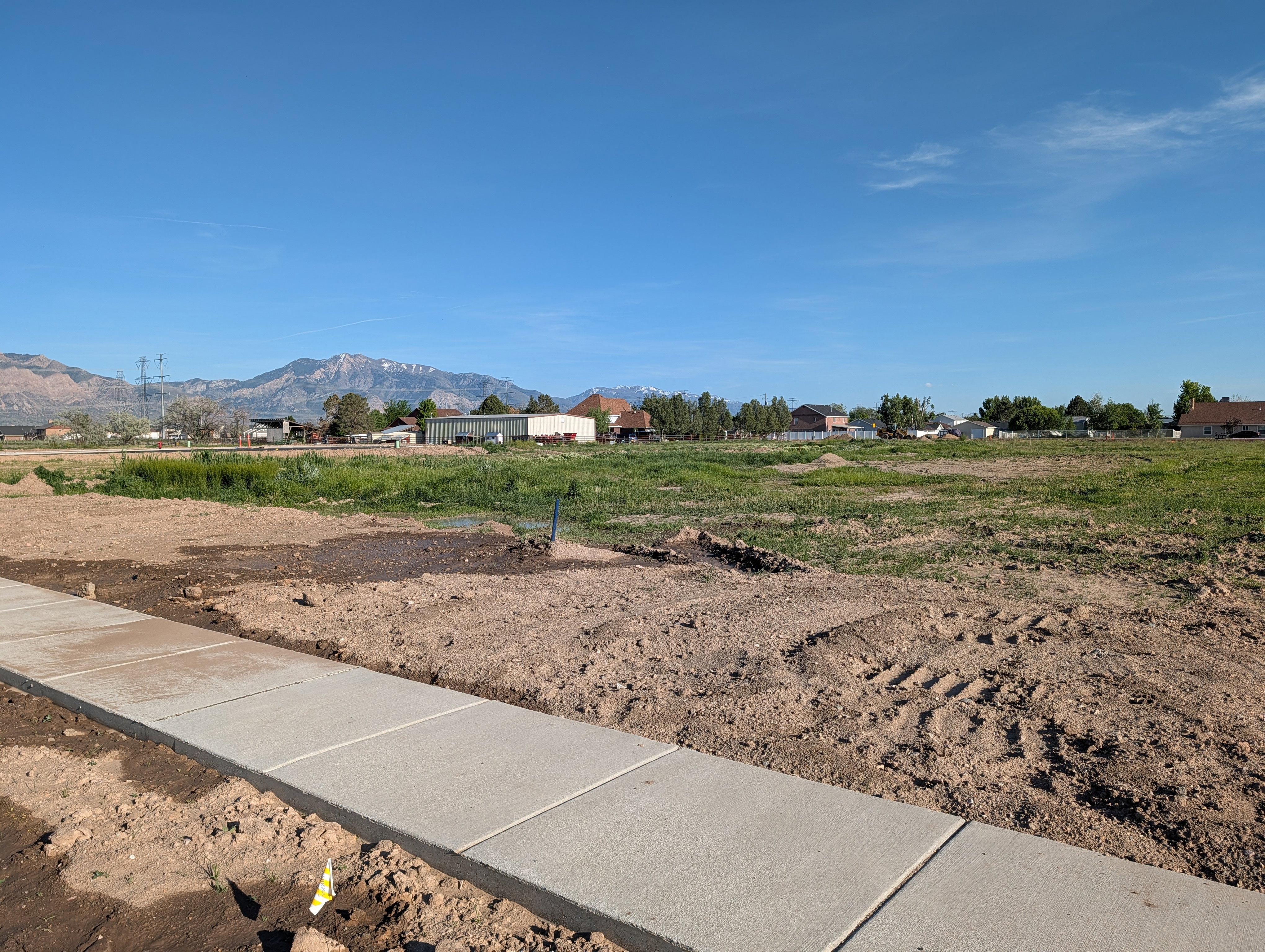Expansive undeveloped parcel featuring a new concrete sidewalk, level terrain, and distant mountain scenery
