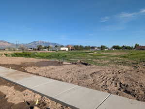 Expansive undeveloped parcel featuring a new concrete sidewalk, level terrain, and distant mountain scenery